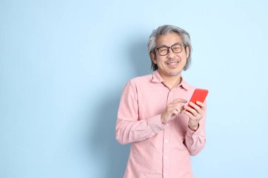 The senior Asian man standing on the blue background with pink shirt.