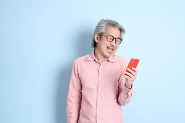 The senior Asian man standing on the blue background with pink shirt.