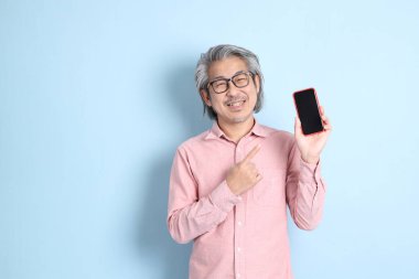 The senior Asian man standing on the blue background with pink shirt.