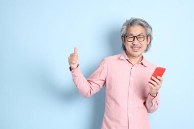 The senior Asian man standing on the blue background with pink shirt.