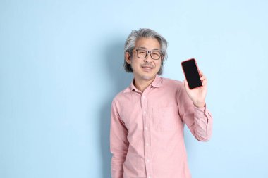 The senior Asian man standing on the blue background with pink shirt.