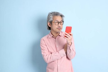 The senior Asian man standing on the blue background with pink shirt.