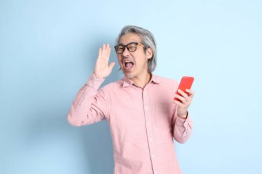 The senior Asian man standing on the blue background with pink shirt.