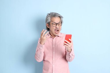 The senior Asian man standing on the blue background with pink shirt.