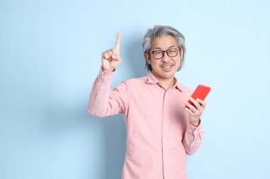 The senior Asian man standing on the blue background with pink shirt.