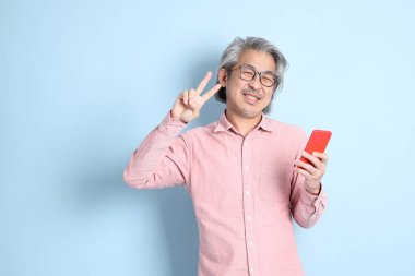 The senior Asian man standing on the blue background with pink shirt.