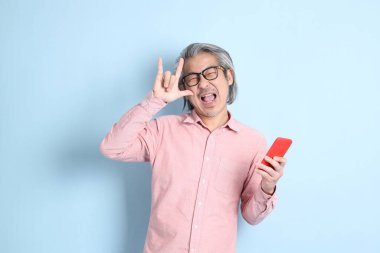 The senior Asian man standing on the blue background with pink shirt.