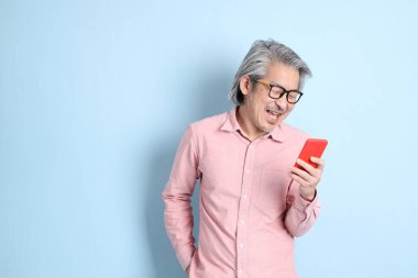 The senior Asian man standing on the blue background with pink shirt.