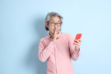 The senior Asian man standing on the blue background with pink shirt.