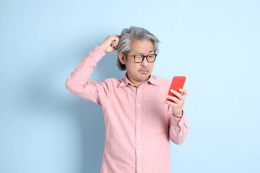 The senior Asian man standing on the blue background with pink shirt.