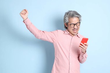 The senior Asian man standing on the blue background with pink shirt.
