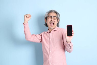 The senior Asian man standing on the blue background with pink shirt.