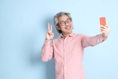 The senior Asian man standing on the blue background with pink shirt.