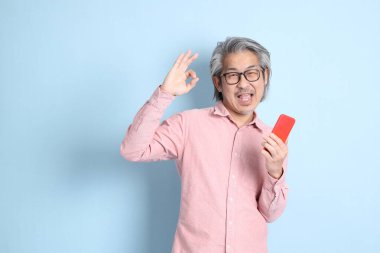 The senior Asian man standing on the blue background with pink shirt.