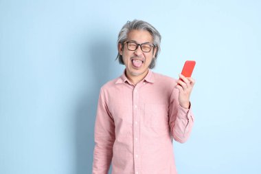 The senior Asian man standing on the blue background with pink shirt.