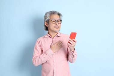 The senior Asian man standing on the blue background with pink shirt.