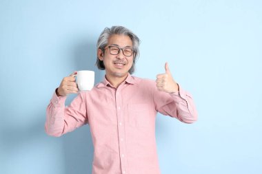 The senior Asian man standing on the blue background with pink shirt.