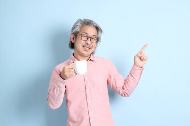 The senior Asian man standing on the blue background with pink shirt.