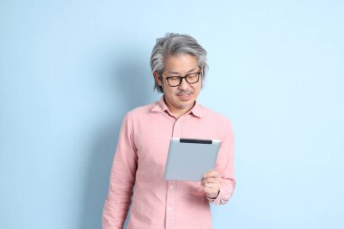The senior Asian man standing on the blue background with pink shirt.