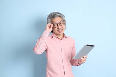 The senior Asian man standing on the blue background with pink shirt.