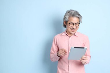 The senior Asian man standing on the blue background with pink shirt.