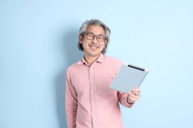 The senior Asian man standing on the blue background with pink shirt.
