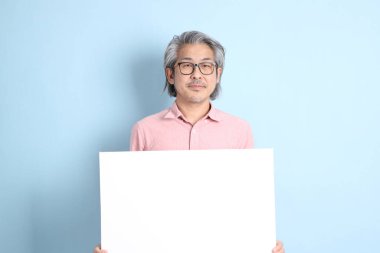 The senior Asian man standing on the blue background with pink shirt.