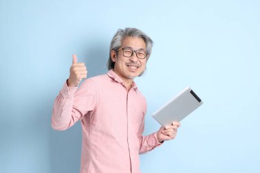 The senior Asian man standing on the blue background with pink shirt.