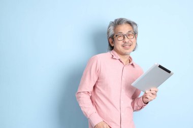 The senior Asian man standing on the blue background with pink shirt.
