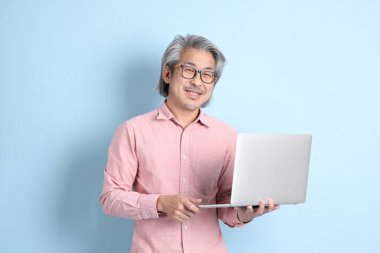 The senior Asian man standing on the blue background with pink shirt.