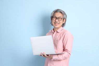 The senior Asian man standing on the blue background with pink shirt.