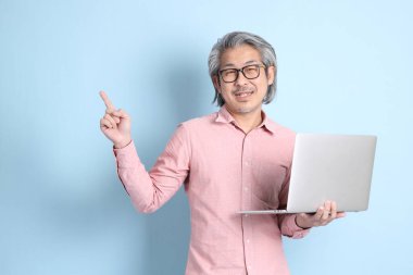 The senior Asian man standing on the blue background with pink shirt.