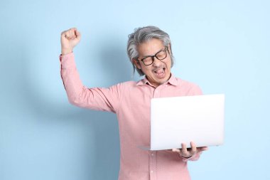 The senior Asian man standing on the blue background with pink shirt.