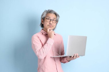 The senior Asian man standing on the blue background with pink shirt.