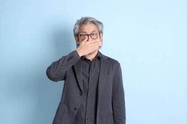 The senior Asian businessman standing on the blue background.