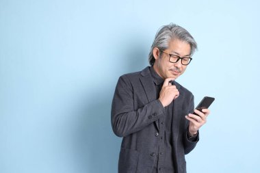 The senior Asian businessman standing on the blue background.
