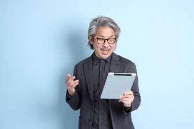 The senior Asian businessman standing on the blue background.