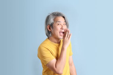 The senior Asian man with yellow t shirt standing on the blue background.