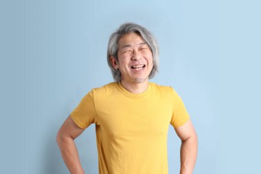 The senior Asian man with yellow t shirt standing on the blue background.