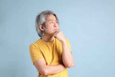 The senior Asian man with yellow t shirt standing on the blue background.