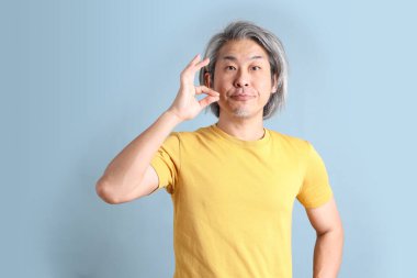 The senior Asian man with yellow t shirt standing on the blue background.