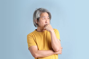 The senior Asian man with yellow t shirt standing on the blue background.
