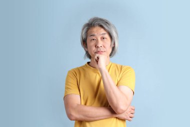 The senior Asian man with yellow t shirt standing on the blue background.