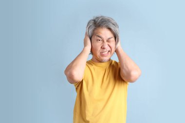 The senior Asian man with yellow t shirt standing on the blue background.