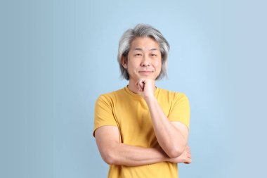 The senior Asian man with yellow t shirt standing on the blue background.