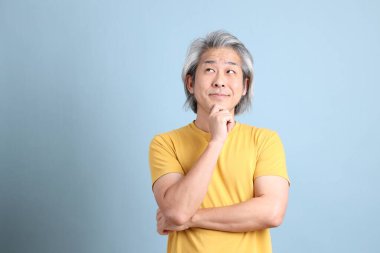 The senior Asian man with yellow t shirt standing on the blue background.