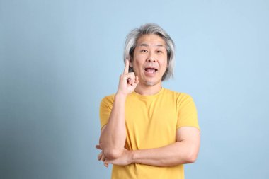 The senior Asian man with yellow t shirt standing on the blue background.