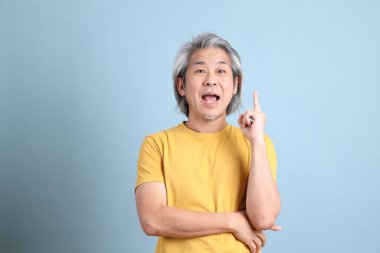 The senior Asian man with yellow t shirt standing on the blue background.