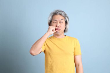 The senior Asian man with yellow t shirt standing on the blue background.