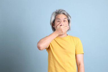 The senior Asian man with yellow t shirt standing on the blue background.